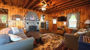 A cozy cabin interior with a stone fireplace, wooden walls, a ceiling fan, and a large rug. - Traditional Waterfront Maine Cottage on Long Lake with great swimming. (Naples)