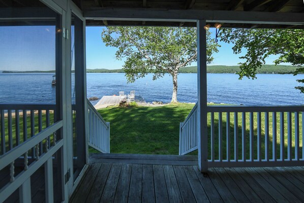 A wooden deck with a view of a lake, a tree, and a dock.