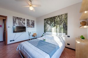 A bedroom with a bed, a desk, a chair, a television, and artwork on the walls.