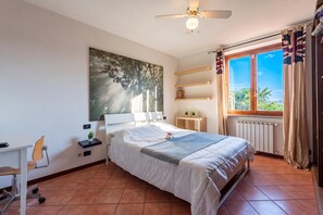 A bedroom with a bed, a desk, a chair, a ceiling fan, a window with curtains, and a radiator. - Homesweethome Lake-view Villetta a Schiera With Garden (Besozzo)