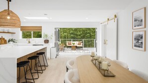 Una cocina moderna con una isla grande, taburetes de bar y un comedor con una mesa de madera y velas.