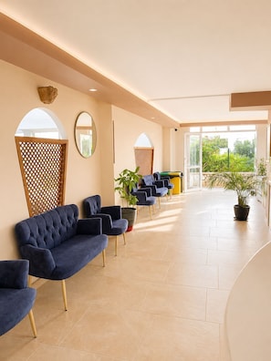 A spacious lobby with a blue sofa, chairs, potted plants, and a view of greenery outside.