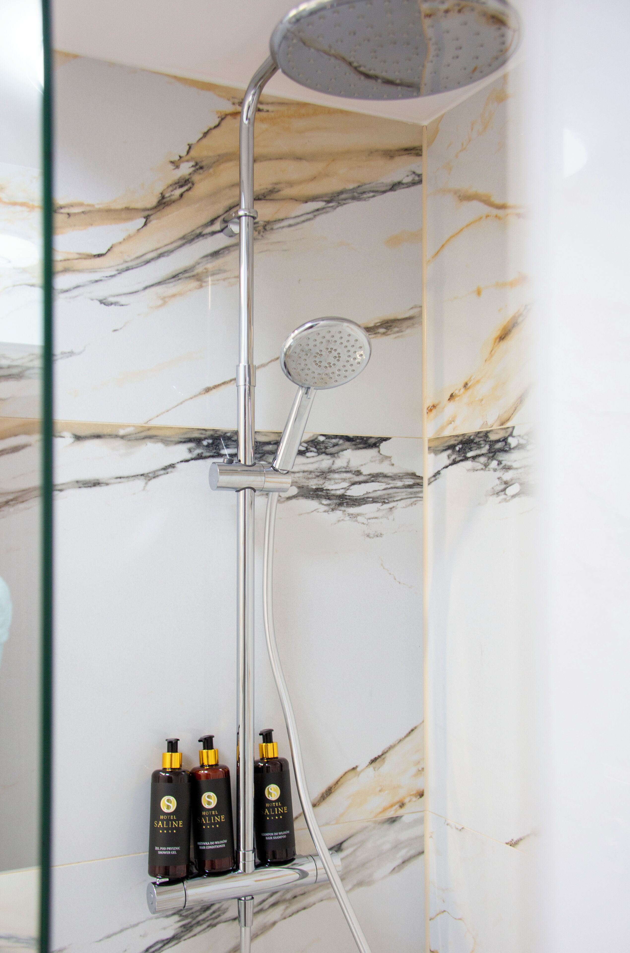 A shower with a rain showerhead and three bottles of hotel toiletries.