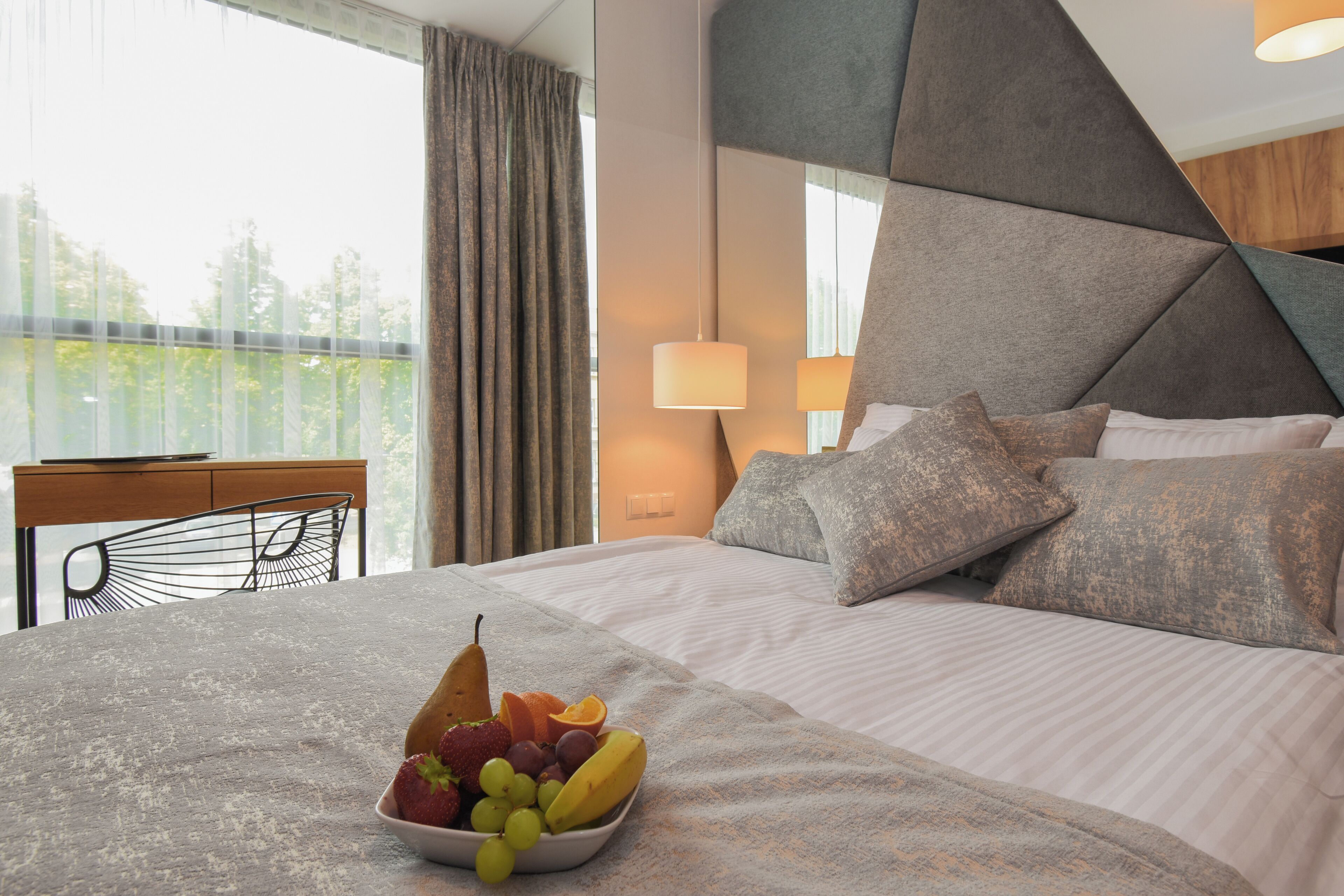 Habitación de hotel moderna con una cama grande, una mesa de comedor y un frutero sobre la cama.
