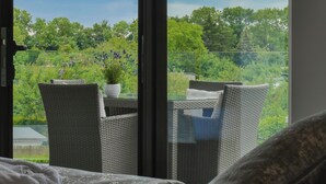 Een balkon met rieten meubels, een plant in pot en uitzicht op groen en bomen.