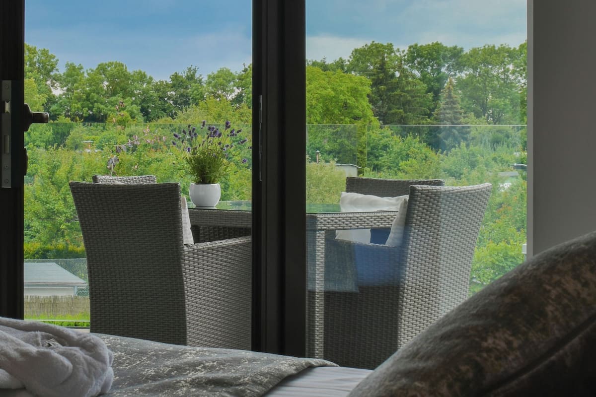 A balcony with wicker furniture, a potted plant, and a view of greenery and trees.