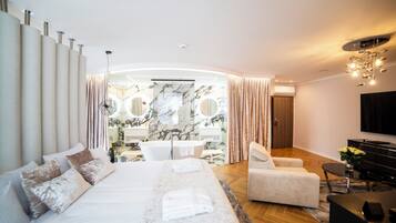 Una habitación de hotel moderna con una cama grande, una zona de estar con sofá y sillón, una mesita y un televisor.