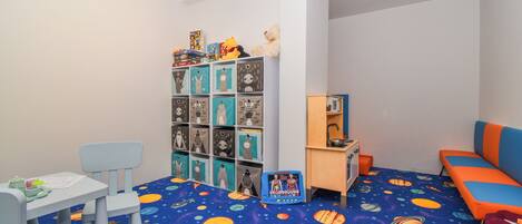 A child's playroom with a space-themed carpet, a bookshelf, a desk, and a couch.