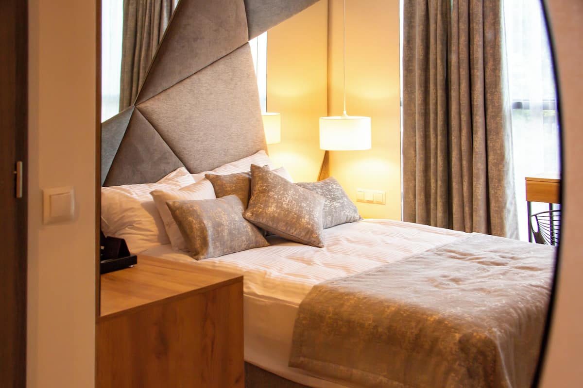 A hotel room with a modern bed, a wooden nightstand, and a lamp.