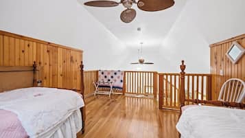 Une chambre avec deux lits, un plancher en bois, un ventilateur de plafond, un balcon avec vue et une balustrade en bois.