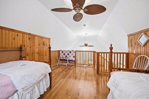 A bedroom with two beds, wooden flooring, a ceiling fan, a balcony with a view, and a wooden railing.