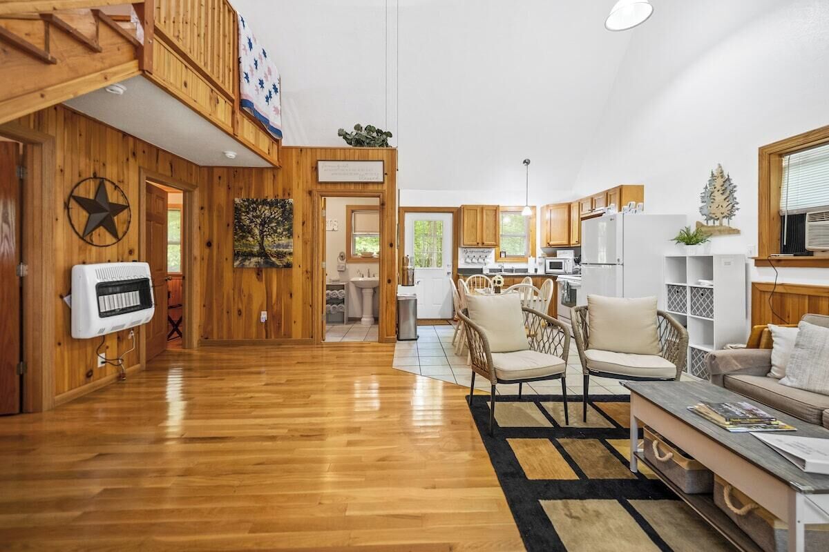 A spacious living area with a wooden floor, a dining area with a white table and chairs, and a kitchen with white cabinets and appliances.