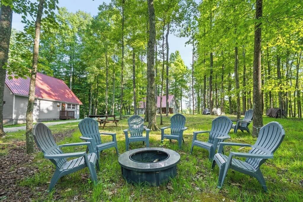 En campingplads med Adirondack-stole placeret omkring et bålsted, omgivet af skov.