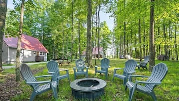 En campingplads med Adirondack-stole placeret omkring et bålsted, omgivet af skov.
