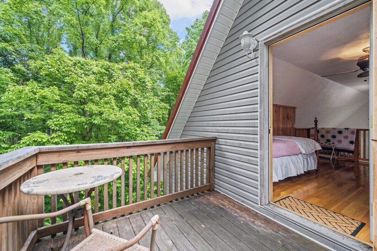 En træterrasse med et bord og stole, et soveværelse med en seng og et natbord, og udsigt til en skov.