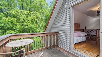 En træterrasse med et bord og stole, et soveværelse med en seng og et natbord, og udsigt til en skov.