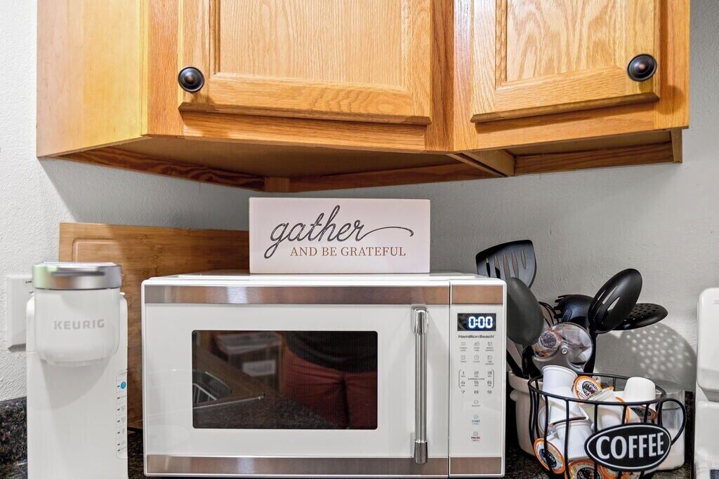 Une cuisine avec des meubles en bois, un four à micro-ondes blanc, une machine à café Keurig et un porte-filtres à café.