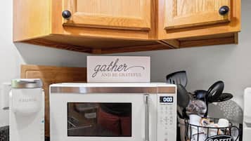 Une cuisine avec des meubles en bois, un four à micro-ondes blanc, une machine à café Keurig et un porte-filtres à café.