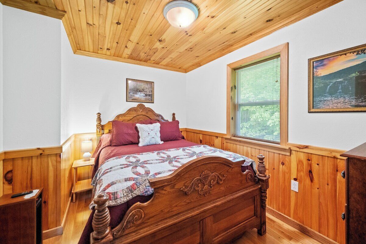 A wooden-paneled bedroom with a bed, a nightstand, a lamp, and a window with a view.