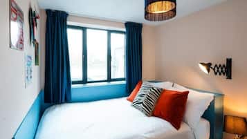 Un dormitorio con cama, ventana y una lámpara fijada a la pared.