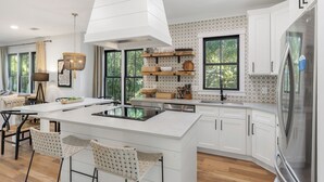 Une cuisine moderne avec des meubles blancs, un îlot central et une grande fenêtre qui laisse entrer la lumière naturelle.