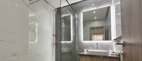 A modern bathroom with a glass-enclosed shower, a vanity with a sink, and a large mirror.