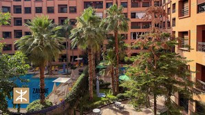 A multi-story residential building with balconies, a swimming pool, and palm trees.