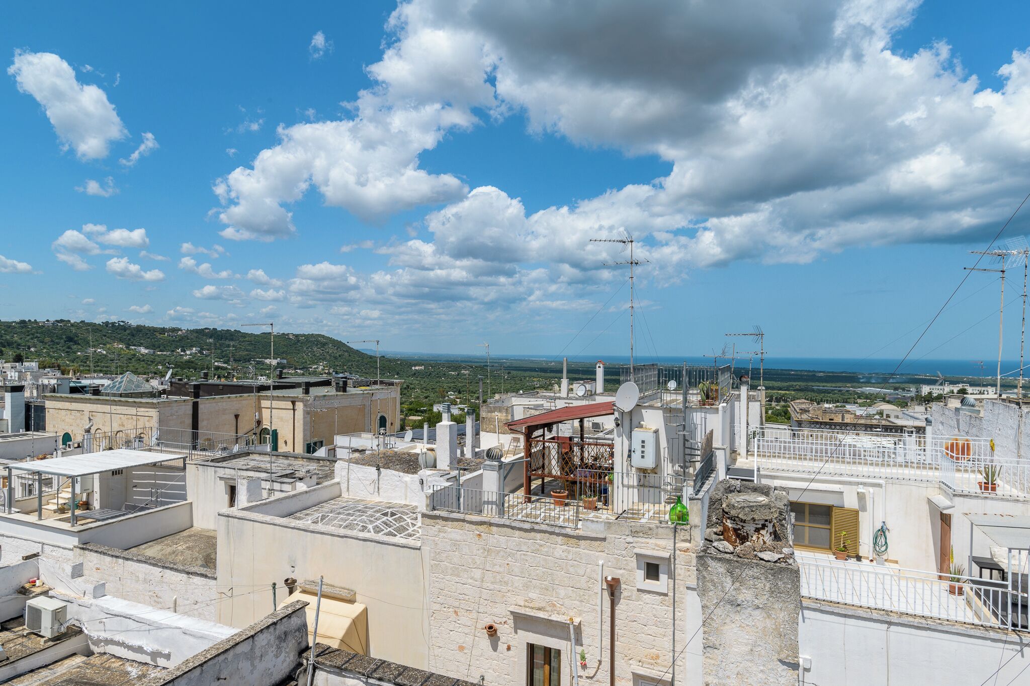 Une terrasse sur le toit, aménagée sur plusieurs niveaux, avec des antennes paraboliques et une vue sur la mer et les collines lointaines.
