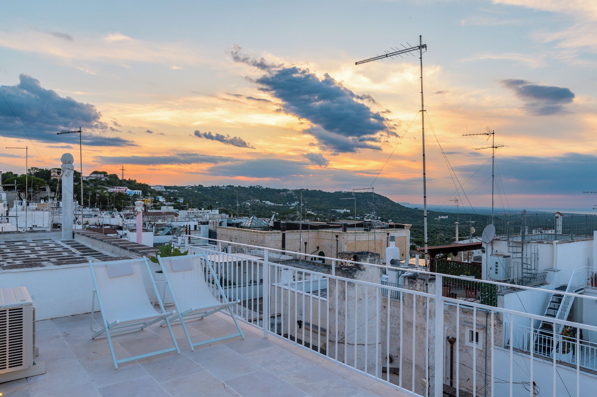 A rooftop terrace with a view of a cityscape during sunset.