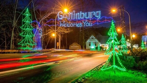 Ein Ortsschild mit 'Gatlinburg Welcomes You' in Neonleuchten, umgeben von Weihnachtsbäumen und Straßenlaternen.