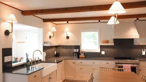Una cocina moderna con una mesa de madera, armarios empotrados, estufa e iluminación colgante.