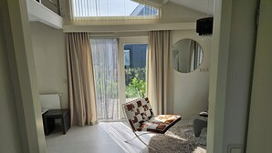 A modern living room with a high ceiling, a large window with curtains, a round mirror, and a patterned sofa. - Beau Su Mer (Kattendijke)