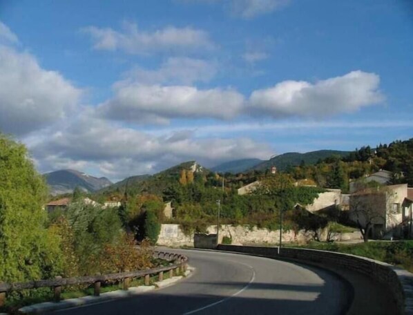 Eine kurvenreiche Straße mit Stein-Geländern, umgeben von Grünflächen und Häusern, unter einem teils bewölkten Himmel.