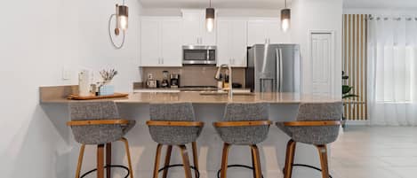 A modern kitchen with white cabinets, stainless steel appliances, and bar stools.