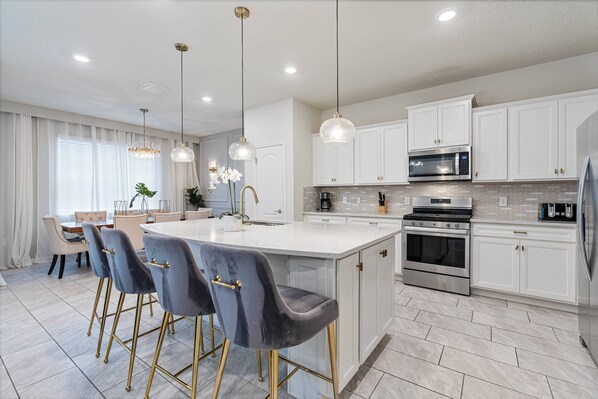 A modern kitchen with white cabinets, a central island with bar stools, stainless steel appliances, and pendant lighting. - 5BR house sleeps 12 with pool table in florida (Davenport)