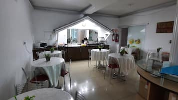 A dining area with round tables, chairs, and a kitchen in the background.