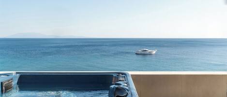 A hot tub on a balcony with a view of the sea and a boat in the distance.