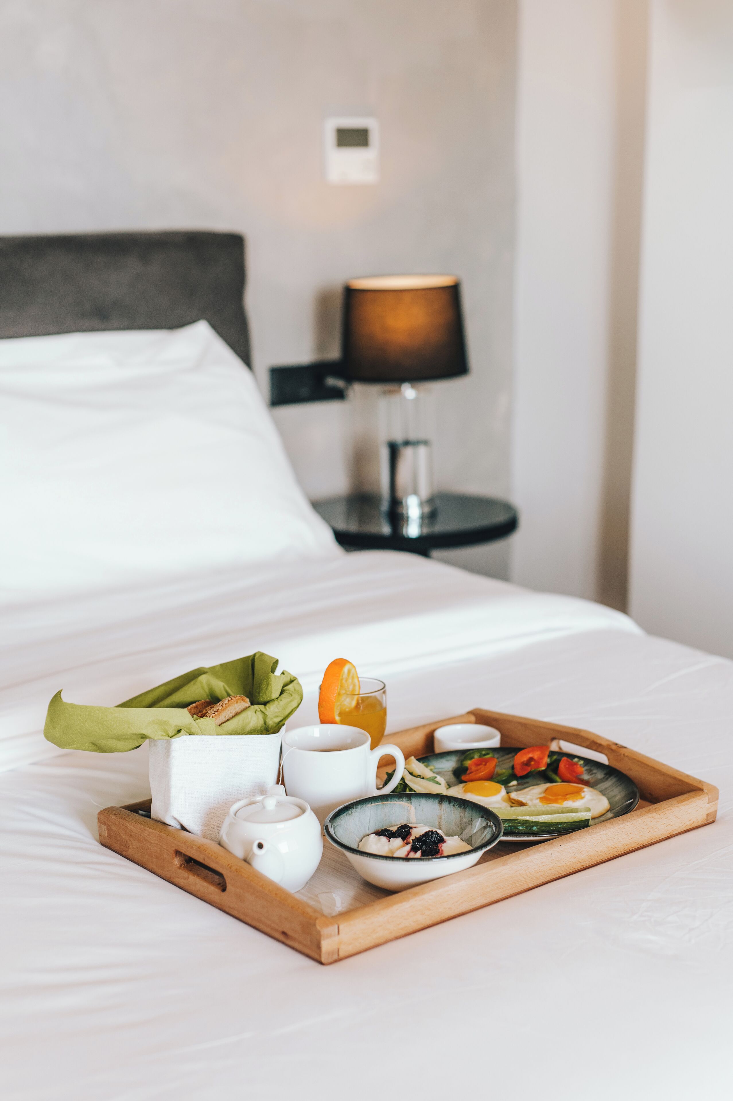 A neatly made breakfast tray with eggs, vegetables, and a cup on a bed.