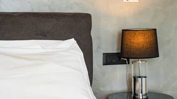 A neatly made bed with a white pillow and a grey headboard. A modern lamp with a dark shade is on a small table beside the bed.
