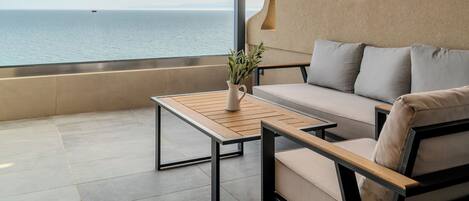 Un área de estar exterior moderna con vista al mar, que incluye un sofá, una mesa de madera y una planta en maceta.