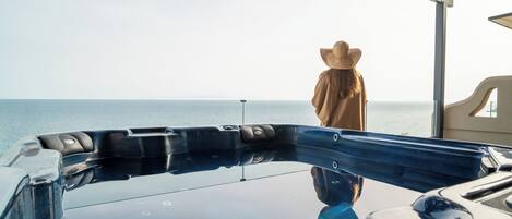 A person standing by a hot tub on a balcony overlooking the sea.