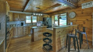 A wooden cabin interior with a kitchen, bar area, and a clock on the wall.