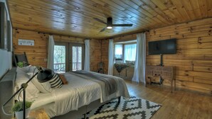 A wooden-paneled bedroom with a bed, a desk, a television, and a ceiling fan.
