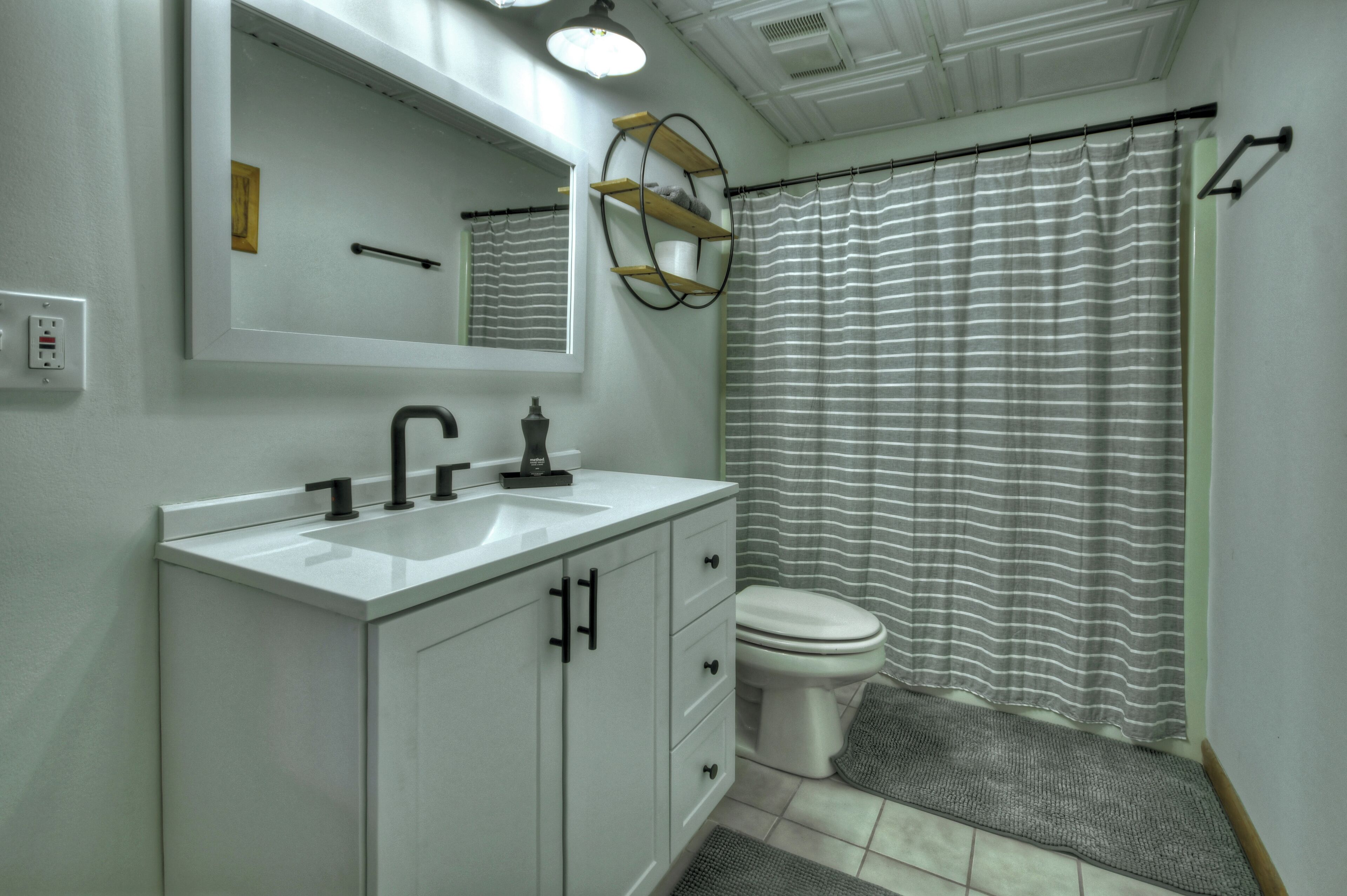 A bathroom with a white sink, black faucet, and a toilet. There is a mirror above the sink and a shower curtain with horizontal stripes.