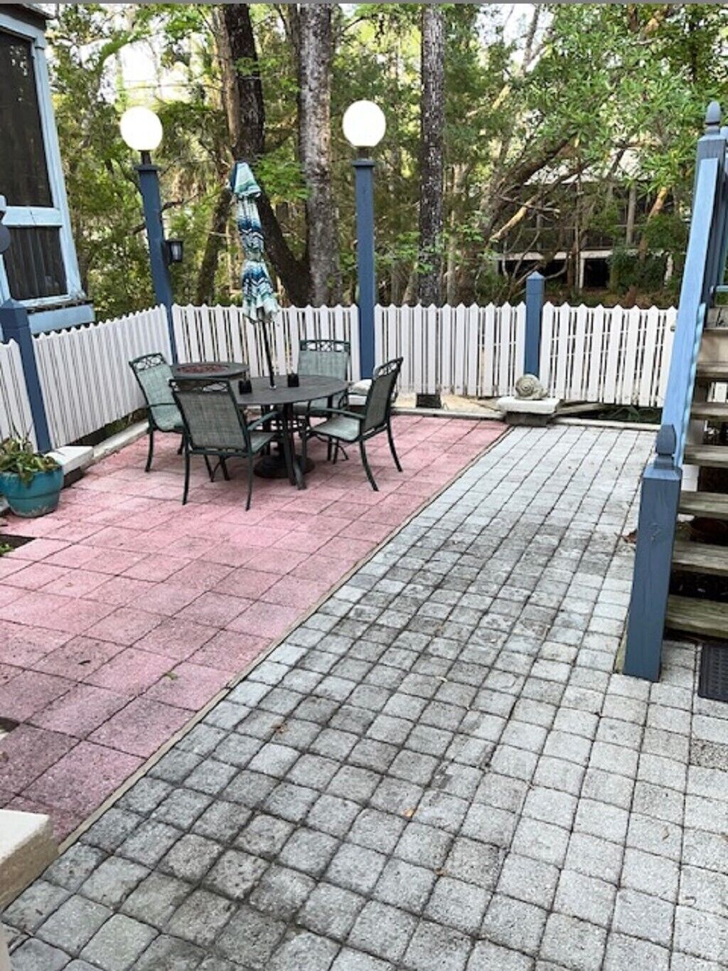 An outdoor patio with a table and chairs, surrounded by a white picket fence and trees.
