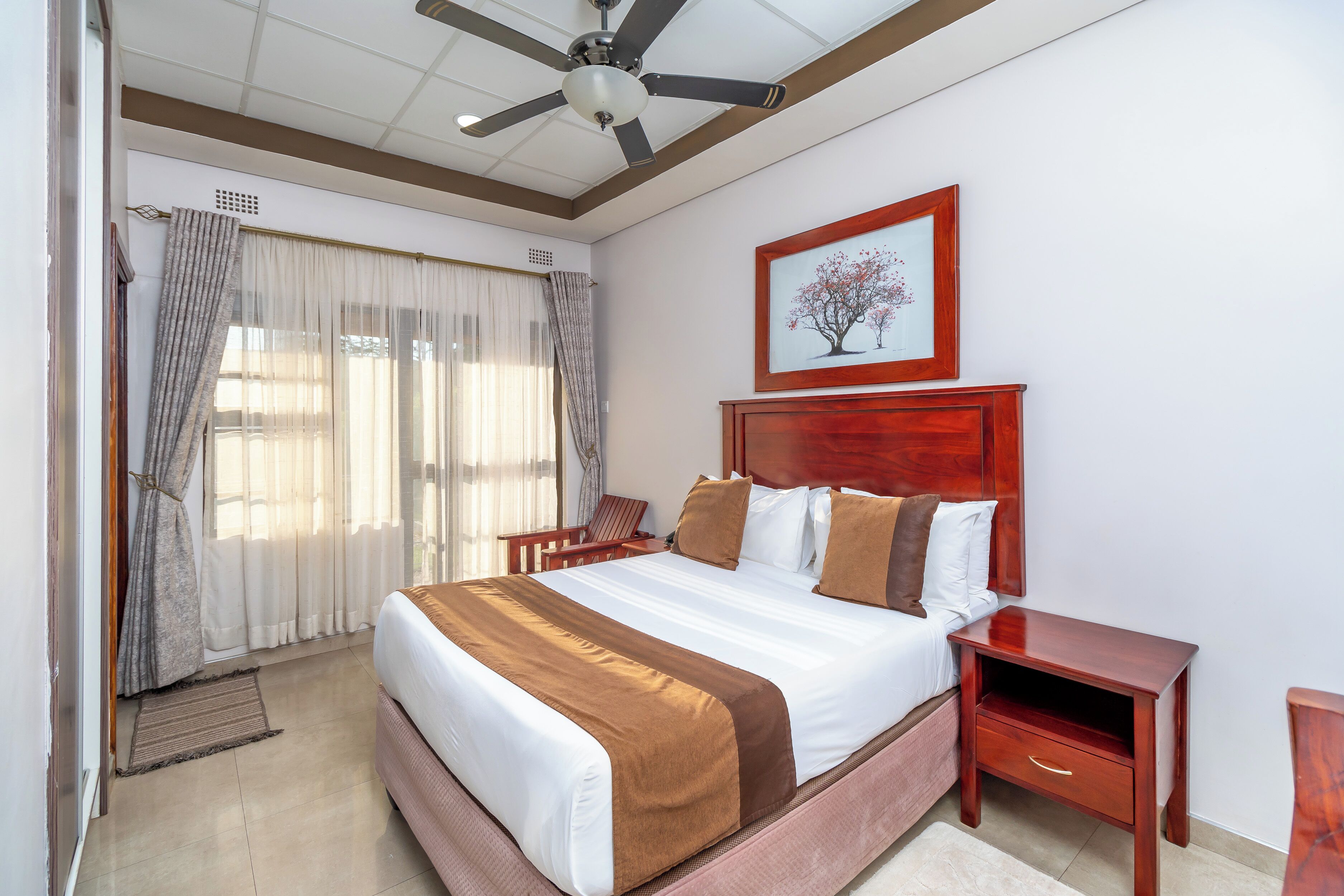 A bedroom with a large bed, a wooden nightstand, a ceiling fan, and a framed picture on the wall.