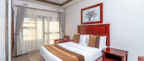 A bedroom with a large bed, a wooden nightstand, a ceiling fan, and a framed picture on the wall.