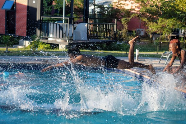 A swimming pool with water splashing, surrounded by a building with a balcony and a lawn. - VTU Platinum Lodge (Turf Town)