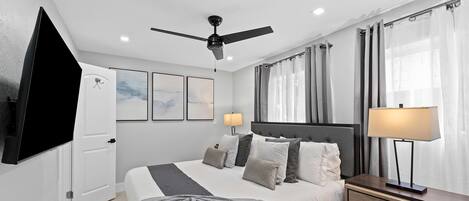 A modern bedroom with a bed, bedside lamps, a ceiling fan, and artwork on the wall.