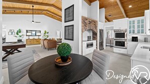 A modern living room with a round table, sofas, a fireplace, and a kitchen area with appliances. - Charming 9BR New-build Home w/ Heated Pool & Games (Hollywood)